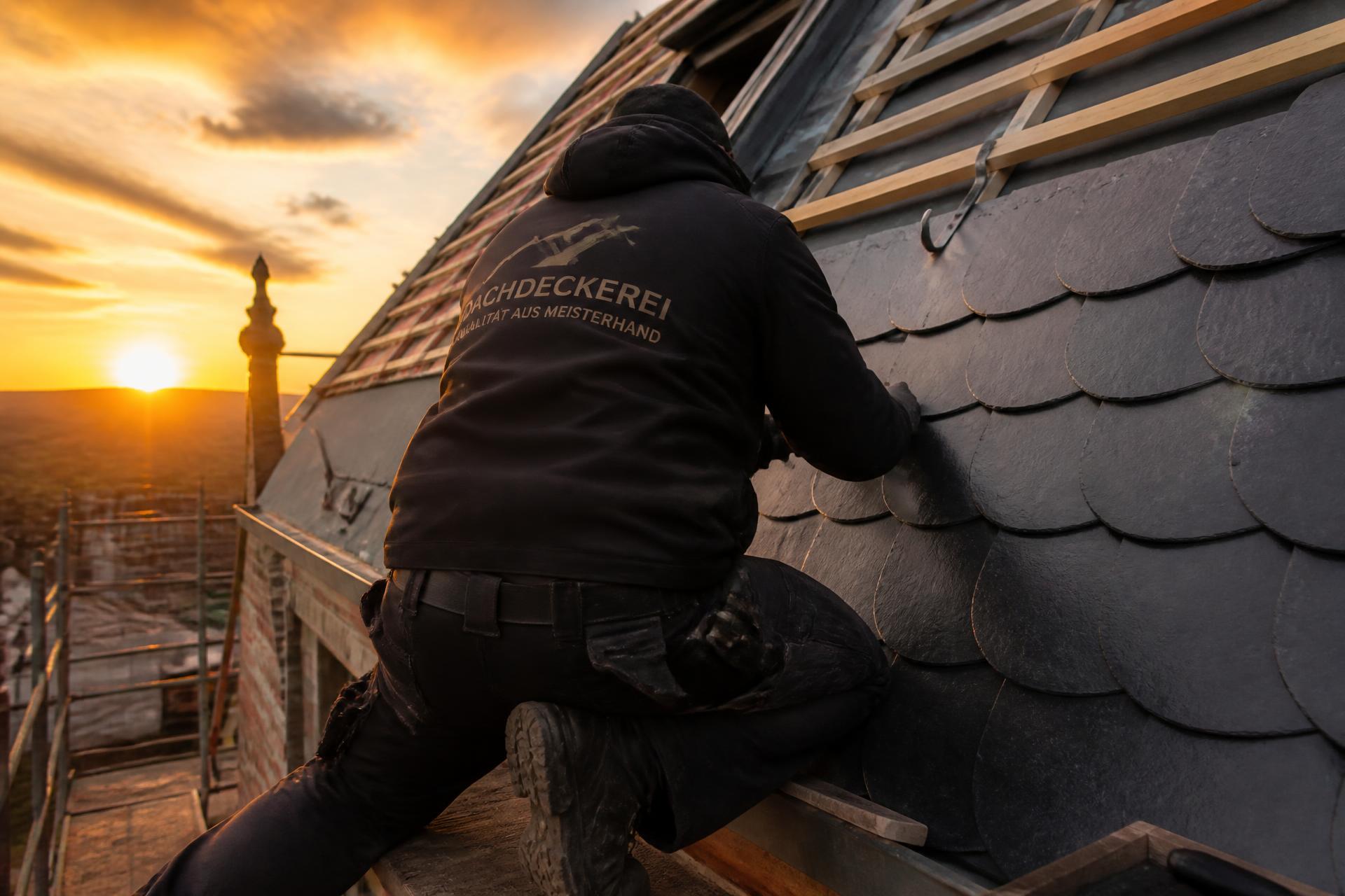 Dachdecker deckt bei Sonnenuntergang ein Steildach mit dunklen Schieferplatten ein